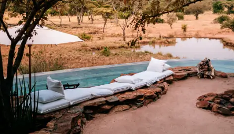 Outside seating area next to a swimming pool looking over a watering hole at a luxury safari leisure accommodation.